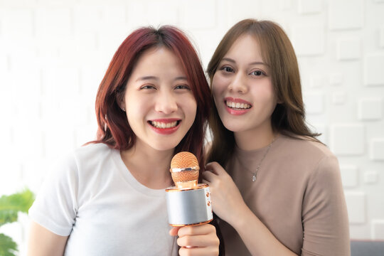 Asian woman holding microphone together in room with smiling.