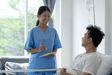 Physiotherapist giving advice and encouragement to male patient doing physiotherapy lying on...