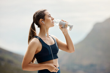 Fitness, woman with earphones, drinking water and hiking in nature for health and wellness during exercise. Music, bottle and fit girl on hike in park for body workout with radio streaming or podcast