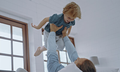 Happy kid boy flying in father's arms in bedroom.father holding raising cute little son playing...