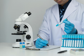 Male scientist using scientific test tubes with data recording of chemicals or drugs tested and examined by microscope in science laboratory for medicine biotechnology biology.