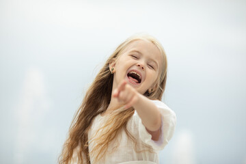 Laughing happy emotional little girl on the sky background pointing at the camera with her finger....