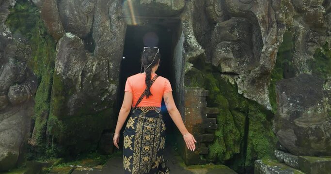 Slow motion shot of a young tourist dressed in a sarong on her journey through the Goa Gajah temple on bali while entering the Goa Gajah elephant cave in ubud indonesia