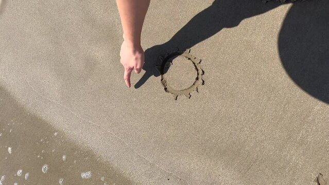 woman drawing a sun in the sand on the beach, vertical view