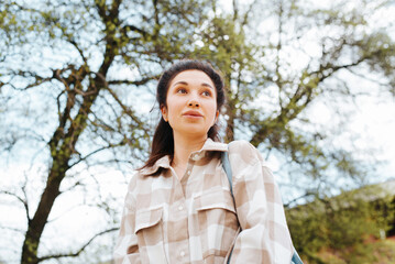 Portrait of a pretty young mixed race woman in casual clothes standing against tree and looking away, low angle view