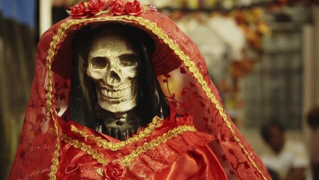 Close up of a skeleton dressed in a red robe with flowers on the head for Día de Muertos - Day of the Dead in Mexico City.
