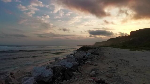 Colorfull sunset at the emtpty beach in Melasti, Uluwatu on the penisula in Bali Indonesia. The sky has beautiful colors and waves roll to the rocky cliff coastline. Steady shot of time before dawn.