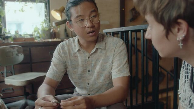Young Asian antique store owner telling history of old pendant to female customer. Over-the-shoulder shot