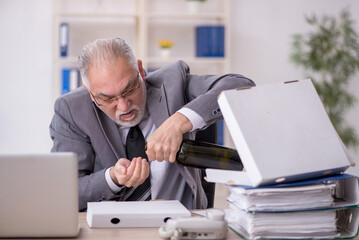 Old male employee drinking alcohol at workplace