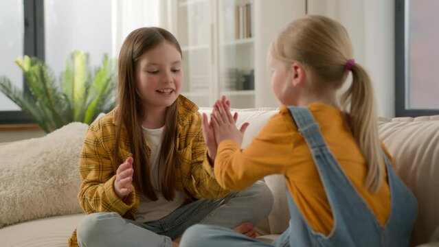 Happy children clapping their hands in living room sofa little cute joyful caucasian kids girls sisters friends playing together at home fun game clap your hands rejoicing enjoying leisure laughing