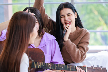 Closeup shot of Millennial two Asian beautiful cheerful female LGBTQ lover couple girlfriends in casual outfit sitting cuddling embracing smiling holding playing guitar singing songs music together