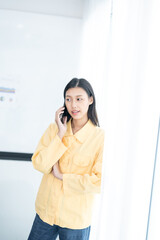 Pretty young Asian business woman standing talking on the phone in the office