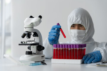 A scientist or medical technician wearing PPE and wearing a glove holds patient-derived blood...