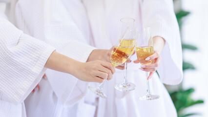 Closeup shot of three tall glasses of sparkling champagne cheering toasting drinking by unrecognizable unknown women in white clean bathrobes celebrating relaxing resting in spa massage studio resort