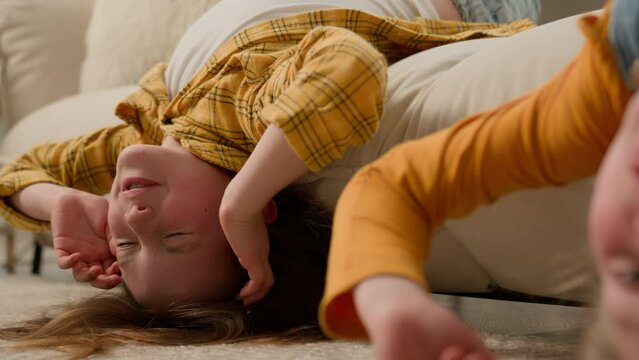 Close-up funny carefree caucasian little kids girls sisters friends playful children having fun together showing tongue fooling around lying upside down on cozy couch in living room enjoying playtime