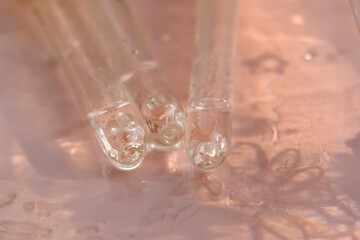 Facial serum or oil dripping from a pipette on a pink background.