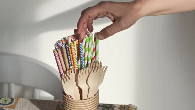 woman's hand chooses biodegradable paper straw from a glass with more sustainable objects. close up image
