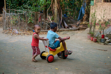 South asian little kids playing with a small tricycle transport in their house yard 