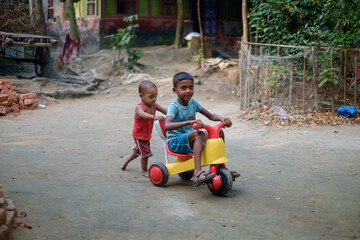 South asian little kids playing with a small tricycle transport in their house yard 