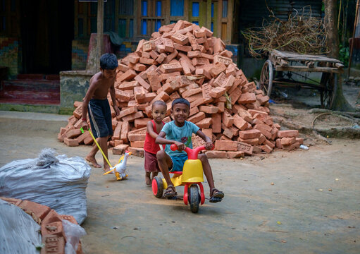 South Asian Little Kids Playing With A Small Tricycle Transport In Their House Yard 