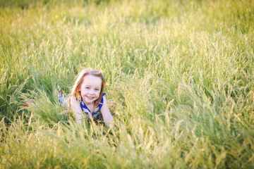 Lovely caucasian girl with long hair lying in long grass at the park with big smile