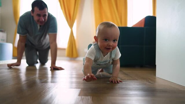 Baby first steps.Toddler at home takes funny first steps.Dad teaches child to walk, legs close-up.Toddler feet on laminate floor.Father's day child education.Kid dream study at home.walk baby learning