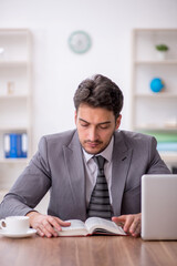 Fototapeta premium Young male employee reading book in the office