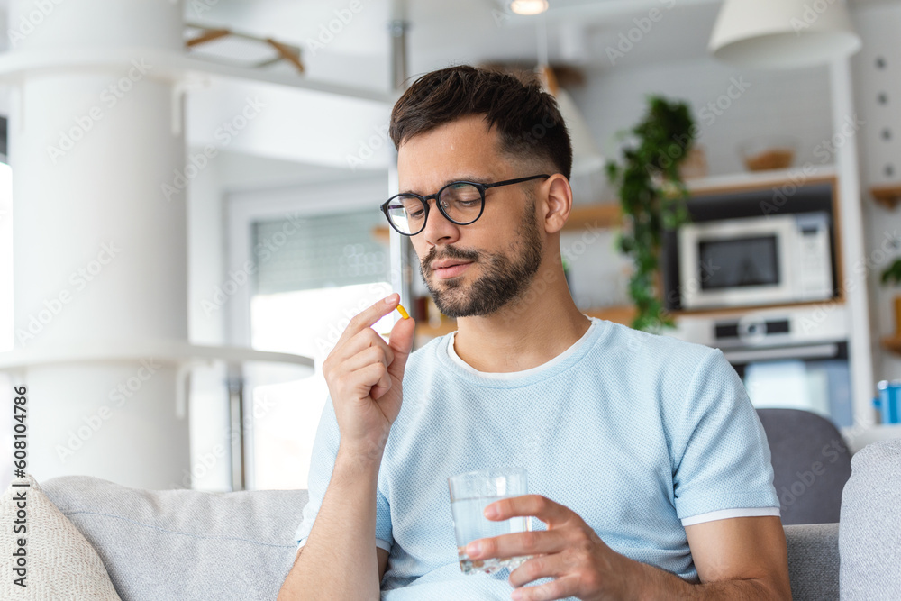 Wall mural young man takes medication prescribed by his physician. man taking a pill and drinking a glass of wa