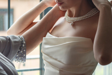 Bride putting on a pearl necklace, mother's hands