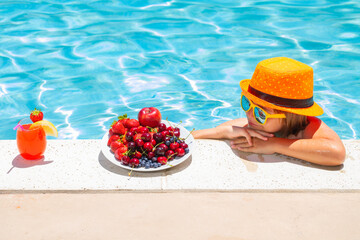 Child eating fruits near swimming pool during summer holidays. Kids eat fruit outdoors. Healthy fruits for children.