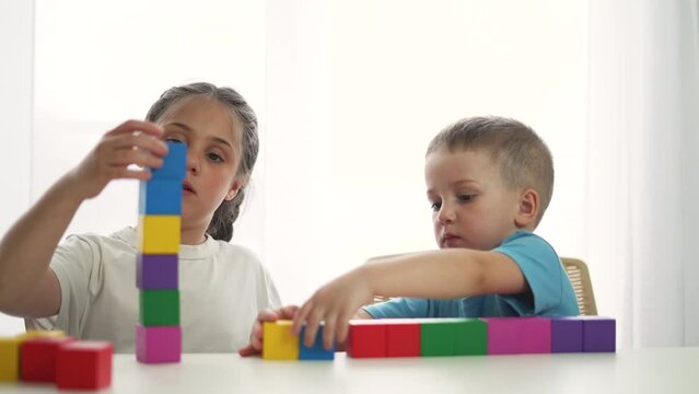 Teamwork of children in kindergarten. Brother and sister play blocks at table in colored toys. Preschool education in kindergarten. Children play with toys. Home games in the family. Home kindergarten