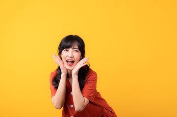 Portrait young beautiful asian woman happy smile dressed in orange clothes looking surprised, reacting amazed, raising eyebrows impressed isolated on yellow studio background.