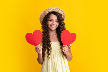 Teenage girl hold shape heart, heart-shape sign. Child holding a red heart love holiday valentine symbol, isolated on yellow background. Happy teenager, positive and smiling emotions of teen girl.