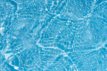 Blue water with ripples on the surface. Defocus blurred transparent blue colored clear calm water surface texture with splashes and bubbles. Water waves with shining pattern texture background.