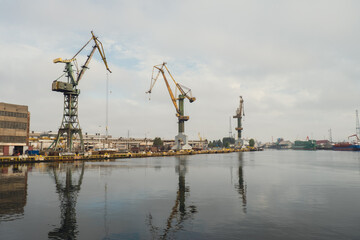 Fototapeta na wymiar Motlawa river to Baltic Sea. Coal mine, polluting environment by the river POV from ferry swimming on river canal. Industrial building at the Gdansk Shipyard. Prefabrication workshop and heavy cranes