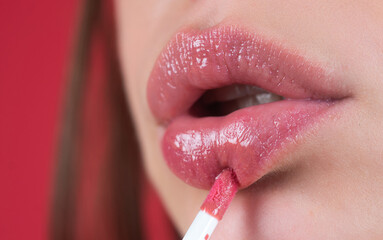 Naklejka premium Applying lipstick, macro. Painting lips with bright lipstick, close up. Pampering, lips correction concept. Glossy lipstick on full plump lip. Woman hand applying lipstick. Lip balm.