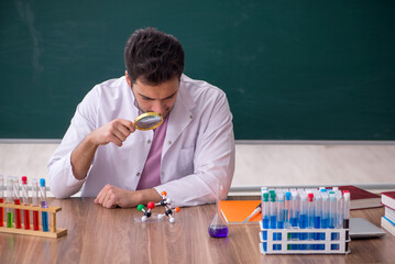 Young male chemistry teacher sitting in the classroom