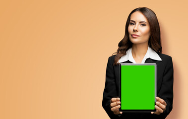 Portrait of young brunette businesswoman showing tablet pc, touchpad, with green chroma key screen, on latte beige background. Confident attractive business woman at office.