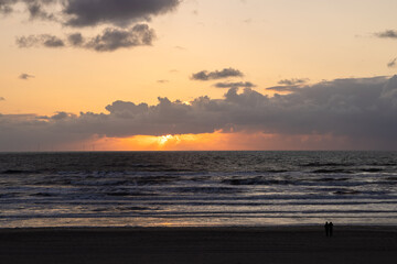 Sunset on the sandy shore of the North Sea in the Netherlands with windmills in background in bokeh