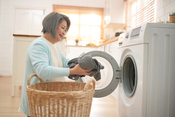 senior housewife doing laundry in the laundry room with clothes inside the washing machine. Domestic life, drying machine, household chores.