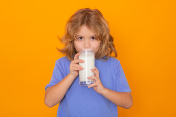 Healthy food for kids. Child with a glass of milk. Cute boy in blue shirt holding glass of milk on yellow isolated studio background. Portrait of funny kid with milk mustache.