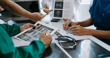 Fototapeta premium Medical team having a meeting with doctors in white lab coats and surgical scrubs seated at a table discussing a patients working online using computers in the medical industry