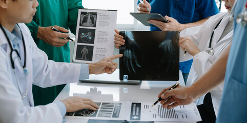 Medical team having a meeting with doctors in white lab coats and surgical scrubs seated at a table discussing a patients working online using computers in the medical industry