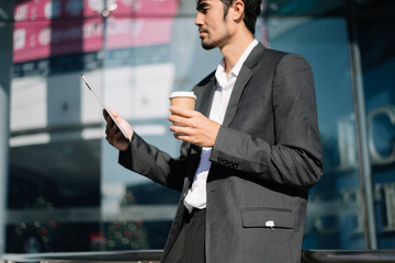 Professional businessman using digital tablet, smartphone and holding coffee to go while working at office