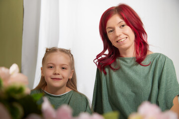 Amazing pretty mother and daughter having fun with flowers in 8 March or in Mother's day. Red haired mom and small little blonde girl having lovely free time on white background