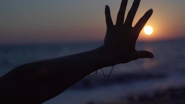 Close-up hand silhouette stretching to red sunset sun. Closeup unrecognizable young woman reaching sundown over Mediterranean sea on Cyprus