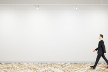 Man walking past blank white wall in modern abstract gallery interior, with empty space for poster or banner, mockup - Powered by Adobe