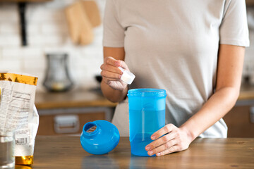 Woman's hand holding scoop while adding protein powder to protein shaker bottle. Body care and...