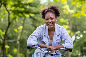 African American woman riding bicycle inside the public park as alternative transport for...