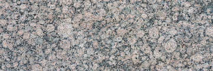 Granite texture. Natural gray granite with a grainy pattern. Stone background. Solid rough surface of rock. Durable construction and decoration material. Close-up.